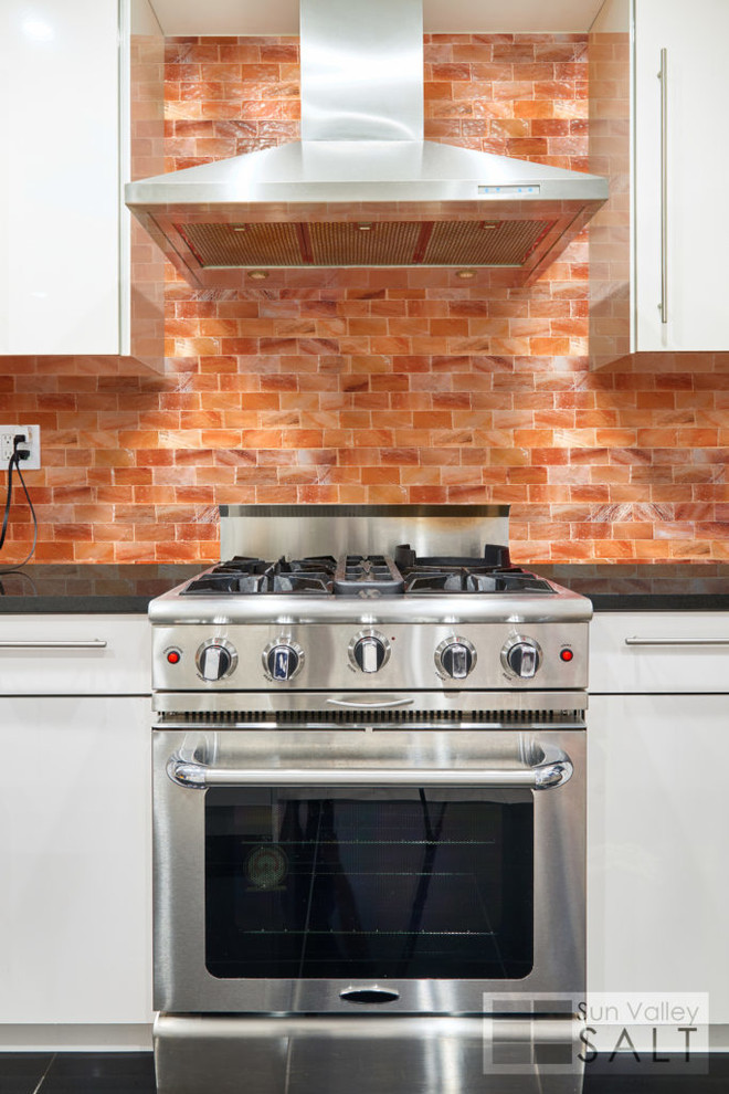Foto di una cucina design di medie dimensioni con ante lisce, ante bianche, top in quarzite, paraspruzzi arancione, elettrodomestici in acciaio inossidabile, pavimento in gres porcellanato e pavimento nero