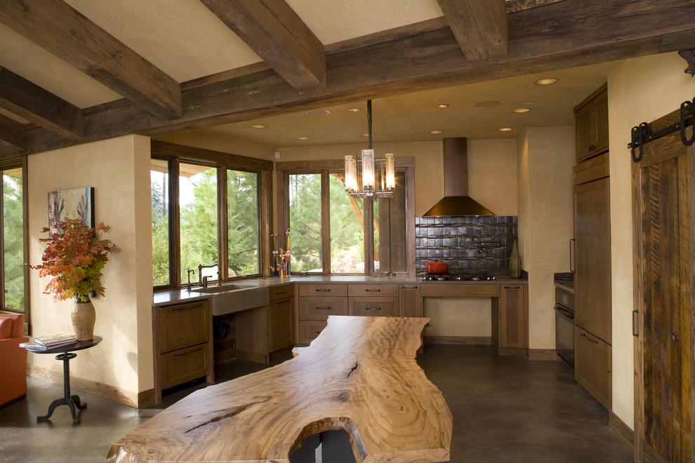 Cette photo montre une cuisine ouverte montagne en U et bois brun de taille moyenne avec un évier de ferme, un placard à porte shaker, un plan de travail en bois, une crédence marron, sol en béton ciré et îlot.
