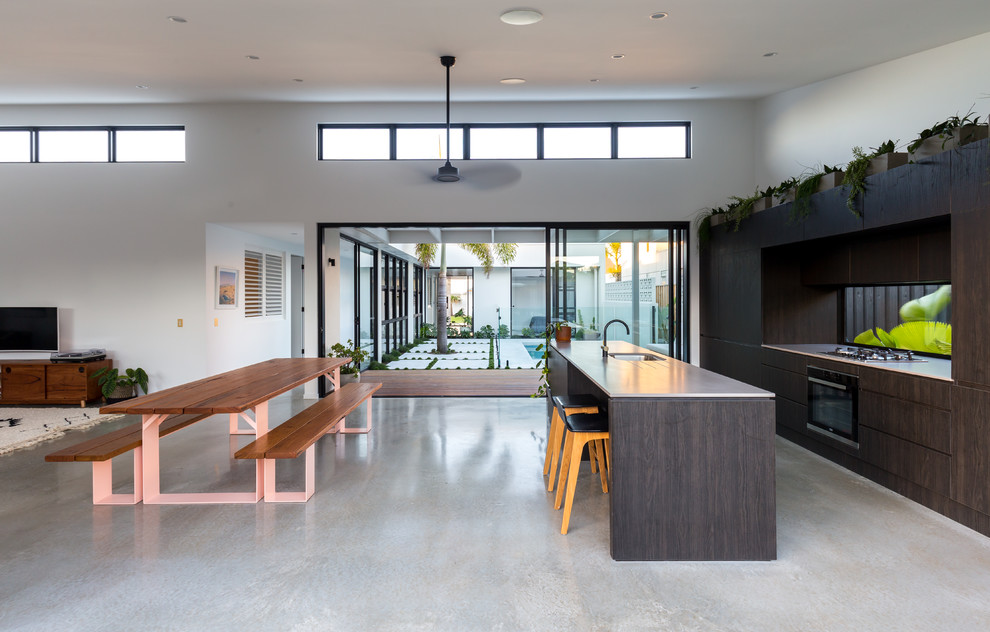 Cette image montre une cuisine ouverte parallèle design en bois foncé avec un évier encastré, un placard à porte plane, fenêtre, sol en béton ciré, îlot, un sol gris et un plan de travail blanc.