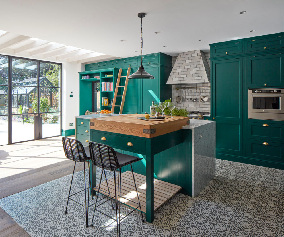 Example of a large transitional l-shaped ceramic tile and multicolored floor kitchen design in London with a farmhouse sink, shaker cabinets, green cabinets, marble countertops, subway tile backsplash, an island, multicolored backsplash and multicolored countertops
