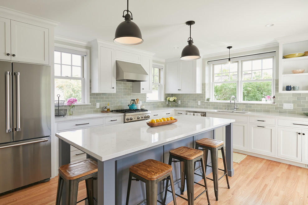 Exemple d'une cuisine chic en L fermée avec un évier 2 bacs, un placard à porte shaker, des portes de placard blanches, un plan de travail en quartz modifié, une crédence verte, une crédence en carreau de porcelaine, un électroménager en acier inoxydable, un sol en bois brun, îlot, un sol marron et un plan de travail blanc.