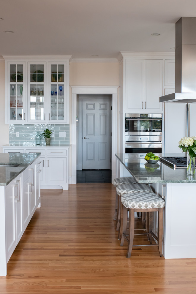 Large trendy l-shaped light wood floor and beige floor open concept kitchen photo in Portland Maine with a farmhouse sink, recessed-panel cabinets, white cabinets, green backsplash, paneled appliances and two islands