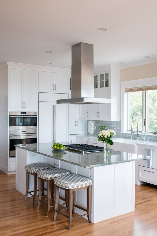 Design ideas for a large contemporary l-shaped open plan kitchen in Portland Maine with a belfast sink, recessed-panel cabinets, white cabinets, green splashback, integrated appliances, light hardwood flooring, multiple islands and beige floors.