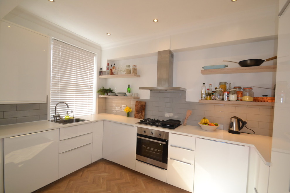 Contemporary u-shaped kitchen in London with a single-bowl sink, flat-panel cabinets, white cabinets, laminate countertops, grey splashback, ceramic splashback and light hardwood flooring.