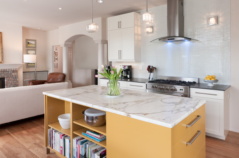 Bild på ett mellanstort funkis kök, med en dubbel diskho, skåp i shakerstil, gula skåp, marmorbänkskiva, vitt stänkskydd, stänkskydd i glaskakel, rostfria vitvaror, ljust trägolv och en köksö
