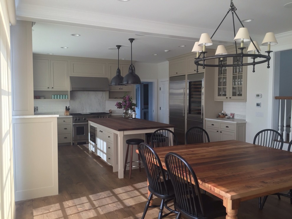 This is an example of a medium sized farmhouse u-shaped kitchen/diner in Burlington with a belfast sink, shaker cabinets, beige cabinets, wood worktops, white splashback, metro tiled splashback, stainless steel appliances, dark hardwood flooring and an island.