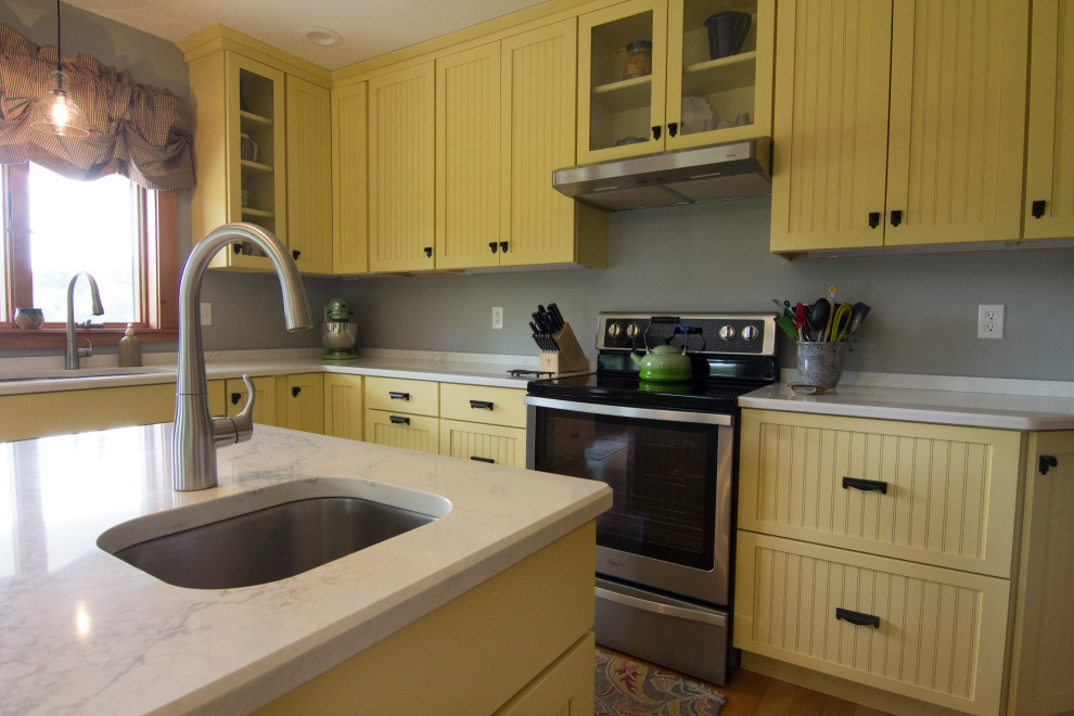 Inredning av ett lantligt mellanstort vit vitt kök, med en undermonterad diskho, luckor med infälld panel, gula skåp, bänkskiva i kvarts, grått stänkskydd, rostfria vitvaror, ljust trägolv, en köksö och orange golv