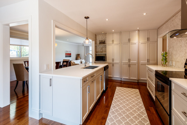 Medium sized traditional galley kitchen/diner in Toronto with a double-bowl sink, beaded cabinets, white cabinets, engineered stone countertops, grey splashback, marble splashback, stainless steel appliances, medium hardwood flooring, an island and brown floors.