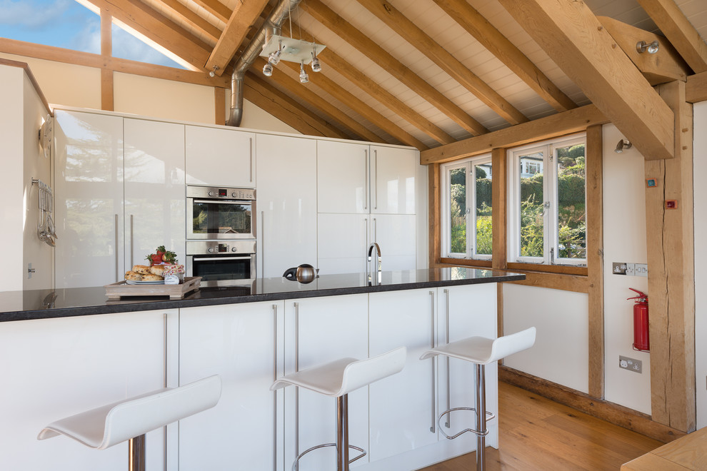 Bild på ett litet funkis kök, med släta luckor, vita skåp, granitbänkskiva, rostfria vitvaror, mellanmörkt trägolv och en köksö