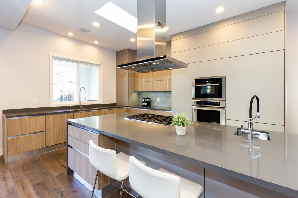 Foto på ett mellanstort funkis grå kök, med en undermonterad diskho, släta luckor, bruna skåp, bänkskiva i kvarts, blått stänkskydd, rostfria vitvaror, mellanmörkt trägolv, en köksö och brunt golv