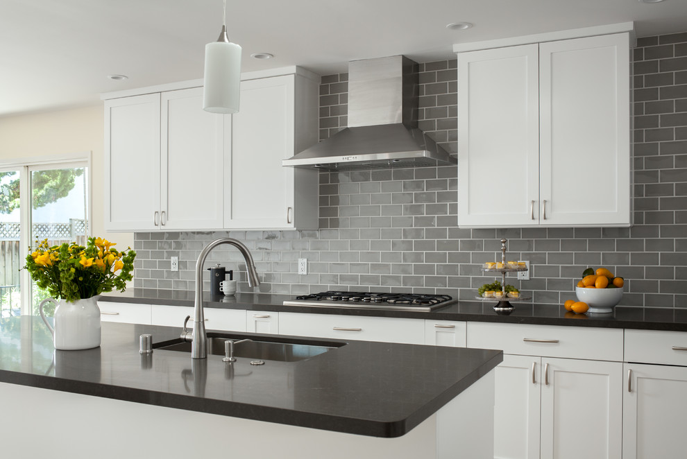 This is an example of a medium sized modern l-shaped kitchen/diner in San Francisco with a built-in sink, white cabinets, quartz worktops, grey splashback, ceramic splashback, stainless steel appliances, light hardwood flooring, an island, beige floors and grey worktops.