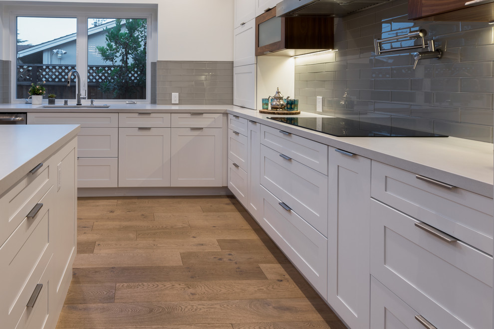 Photo of a large contemporary l-shaped kitchen in San Francisco with a submerged sink, shaker cabinets, white cabinets, grey splashback, glass tiled splashback, stainless steel appliances, medium hardwood flooring, an island, brown floors, white worktops and concrete worktops.