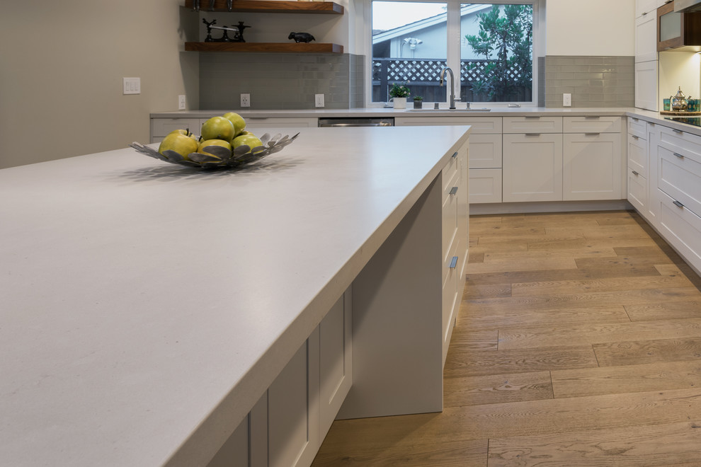 Inspiration for a large contemporary l-shaped kitchen in San Francisco with a submerged sink, shaker cabinets, white cabinets, grey splashback, glass tiled splashback, stainless steel appliances, medium hardwood flooring, an island, brown floors, white worktops and concrete worktops.