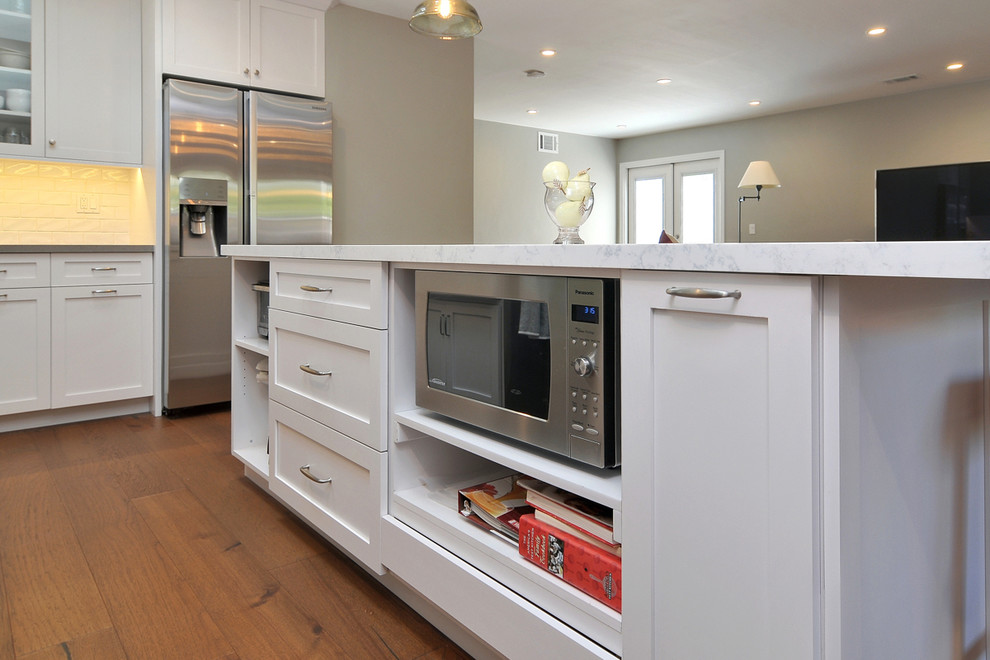 Exempel på ett klassiskt kök, med en rustik diskho, skåp i shakerstil, vita skåp, bänkskiva i kvarts, vitt stänkskydd, stänkskydd i tunnelbanekakel, rostfria vitvaror, mellanmörkt trägolv och en köksö