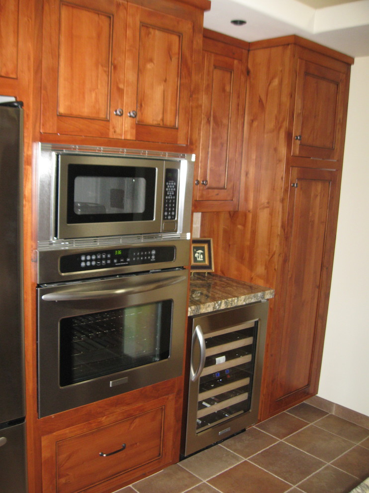 Bild på ett amerikanskt kök, med en undermonterad diskho, luckor med profilerade fronter, skåp i mörkt trä, granitbänkskiva, beige stänkskydd, stänkskydd i keramik, rostfria vitvaror, skiffergolv och en köksö
