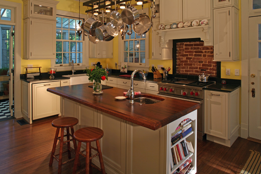 Example of a mid-sized farmhouse u-shaped dark wood floor eat-in kitchen design in St Louis with a drop-in sink, raised-panel cabinets, white cabinets, wood countertops, red backsplash, brick backsplash, stainless steel appliances and an island