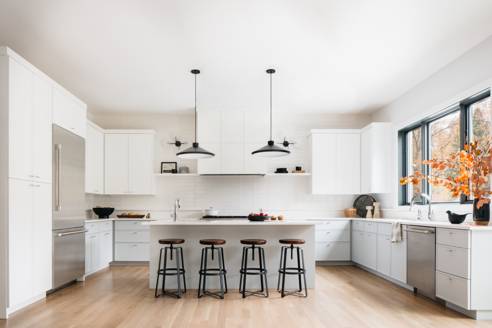 Cette image montre une cuisine design en U avec des portes de placard blanches, un électroménager en acier inoxydable, parquet clair, îlot, un sol beige et un plan de travail blanc.