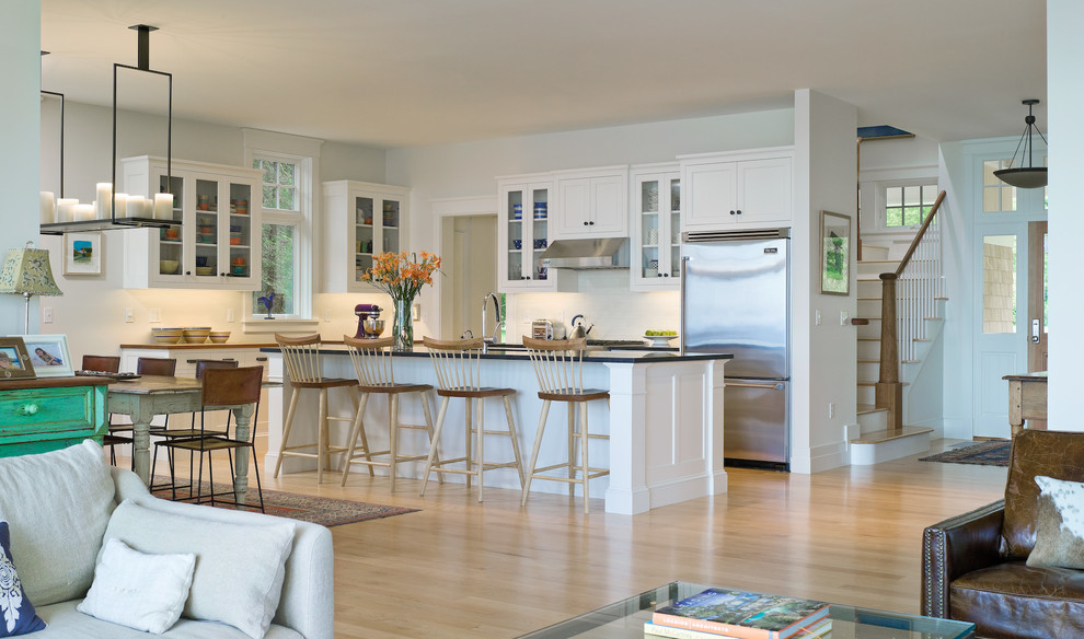 Inspiration for a large classic l-shaped open plan kitchen in Burlington with a single-bowl sink, glass-front cabinets, white cabinets, stainless steel appliances, light hardwood flooring and an island.