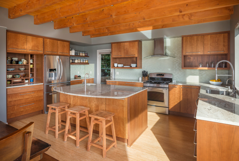 Foto på ett funkis kök, med en undermonterad diskho, släta luckor, skåp i mellenmörkt trä, bambugolv, grönt stänkskydd, stänkskydd i glaskakel och rostfria vitvaror