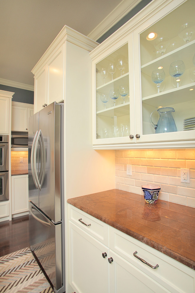Cette image montre une cuisine traditionnelle avec un placard à porte vitrée, des portes de placard beiges, une crédence beige et un électroménager en acier inoxydable.