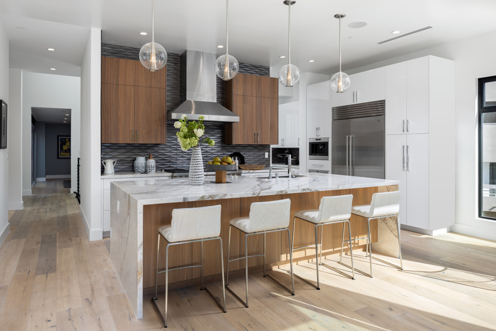 Trendy l-shaped light wood floor and beige floor kitchen photo in Other with an undermount sink, flat-panel cabinets, white cabinets, gray backsplash, stainless steel appliances, an island and white countertops