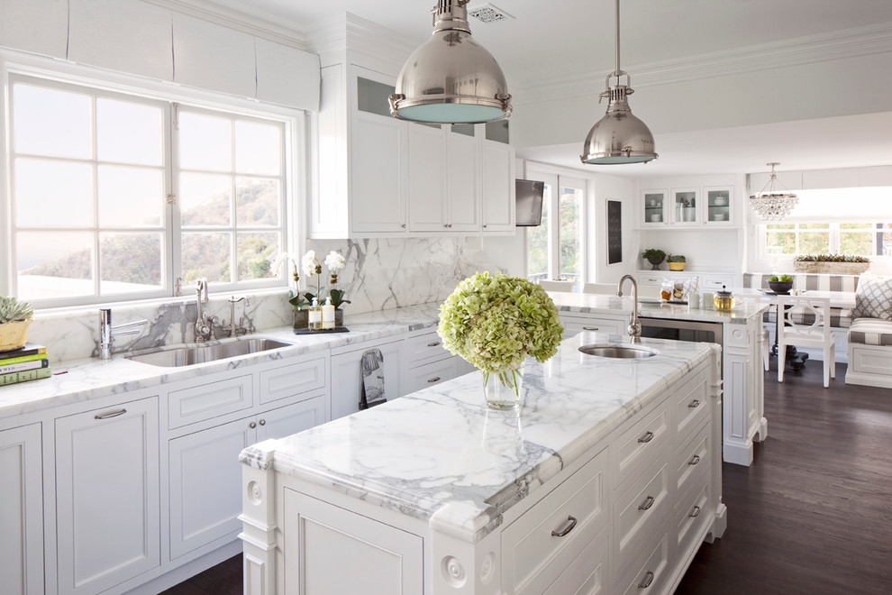 Inspiration for a mid-sized timeless l-shaped dark wood floor and brown floor eat-in kitchen remodel in Los Angeles with an undermount sink, recessed-panel cabinets, white cabinets, white backsplash, marble countertops, stone slab backsplash, stainless steel appliances and an island