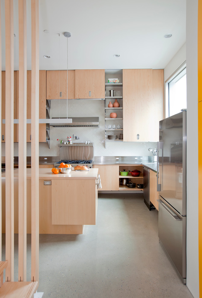 Moderne Küche in L-Form mit flächenbündigen Schrankfronten, hellen Holzschränken, Küchengeräten aus Edelstahl, Betonboden, Kücheninsel und Edelstahl-Arbeitsplatte in Vancouver
