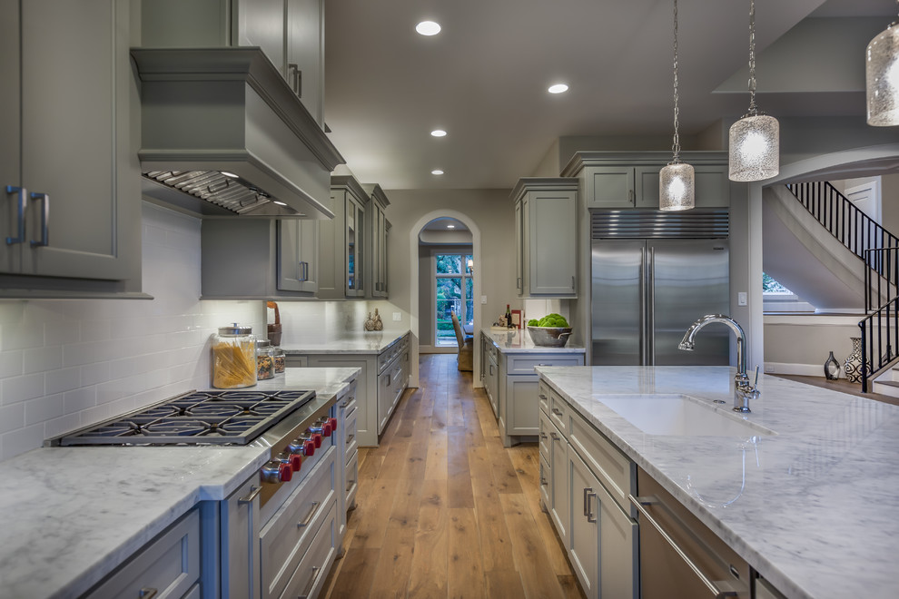 Inspiration for a huge transitional single-wall light wood floor and brown floor kitchen remodel in Houston with a drop-in sink, recessed-panel cabinets, gray cabinets, marble countertops, white backsplash, subway tile backsplash, white appliances, an island and gray countertops