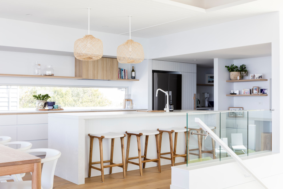 Design ideas for a nautical galley kitchen in Sunshine Coast with flat-panel cabinets, white cabinets, black appliances, medium hardwood flooring, an island, brown floors and white worktops.