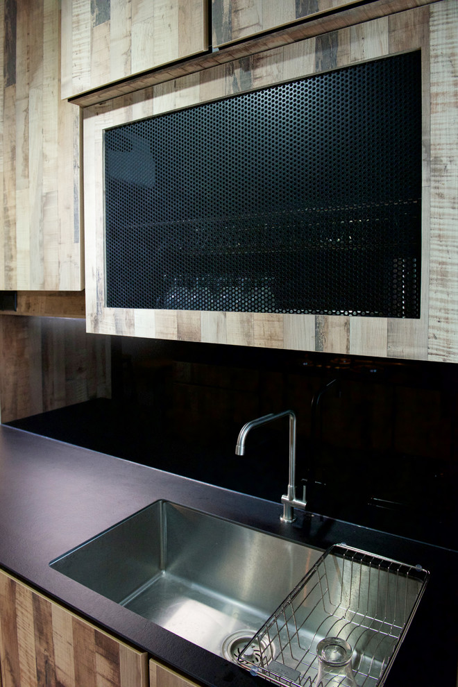 Cette photo montre une arrière-cuisine industrielle en bois brun avec un évier 1 bac, une crédence noire et une crédence en feuille de verre.
