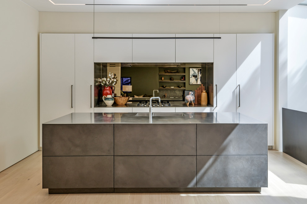 Contemporary kitchen in London with an integrated sink, flat-panel cabinets, white cabinets, stainless steel worktops, mirror splashback, light hardwood flooring, an island and beige floors.