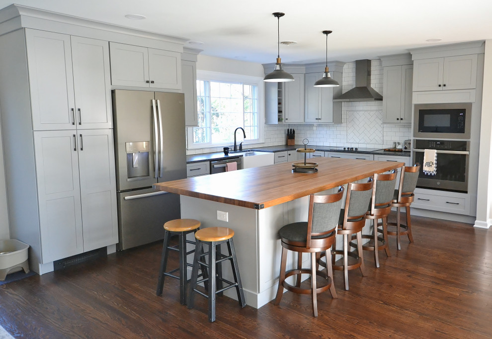 Example of a large transitional l-shaped dark wood floor and brown floor eat-in kitchen design in Philadelphia with a farmhouse sink, recessed-panel cabinets, white cabinets, wood countertops, white backsplash, subway tile backsplash, stainless steel appliances, an island and multicolored countertops