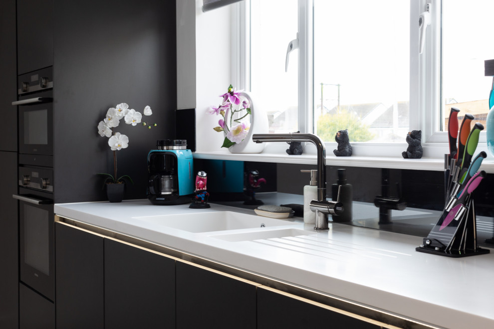 Example of a mid-sized minimalist l-shaped light wood floor and gray floor eat-in kitchen design in Edinburgh with a double-bowl sink, flat-panel cabinets, black cabinets, black backsplash, glass sheet backsplash, black appliances, a peninsula and black countertops