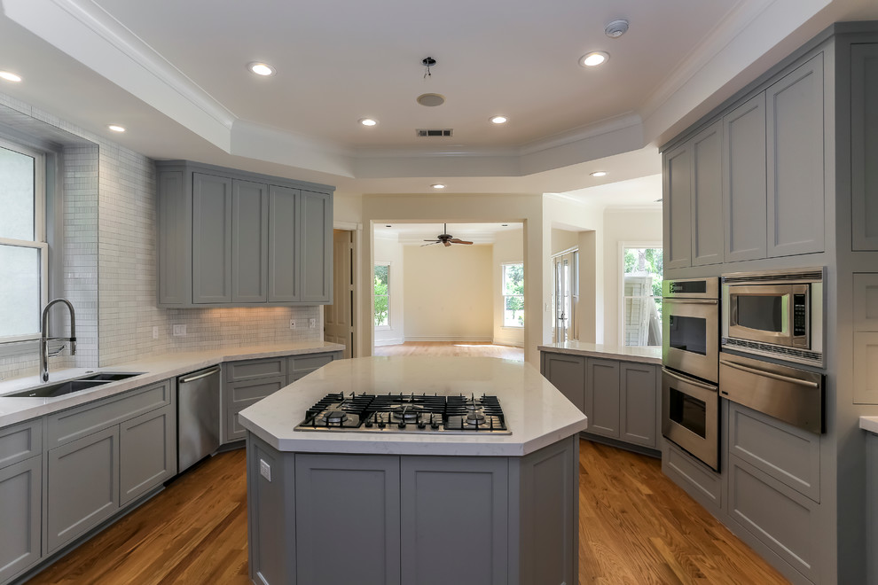Large transitional u-shaped medium tone wood floor and brown floor enclosed kitchen photo in Houston with a double-bowl sink, recessed-panel cabinets, gray cabinets, quartzite countertops, gray backsplash, stainless steel appliances and an island