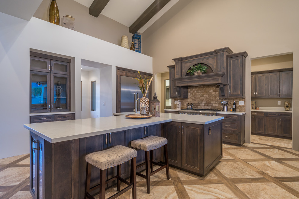 Modelo de cocina tradicional, de tamaño medio, con fregadero sobremueble, armarios con paneles empotrados, puertas de armario de madera oscura, encimera de cuarcita, salpicadero de azulejos de piedra, electrodomésticos de acero inoxidable, suelo de baldosas de porcelana, una isla y salpicadero beige