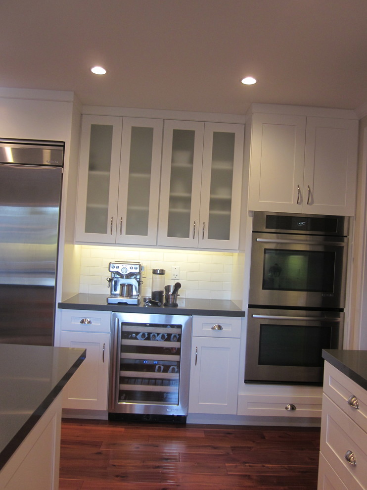 Example of a large trendy u-shaped dark wood floor eat-in kitchen design in Los Angeles with a single-bowl sink, shaker cabinets, white cabinets, quartz countertops, white backsplash, ceramic backsplash, stainless steel appliances and an island
