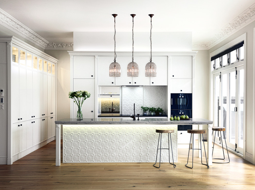 Design ideas for a large victorian l-shaped kitchen in Auckland with a belfast sink, raised-panel cabinets, white cabinets, quartz worktops, white splashback, black appliances, light hardwood flooring and multiple islands.