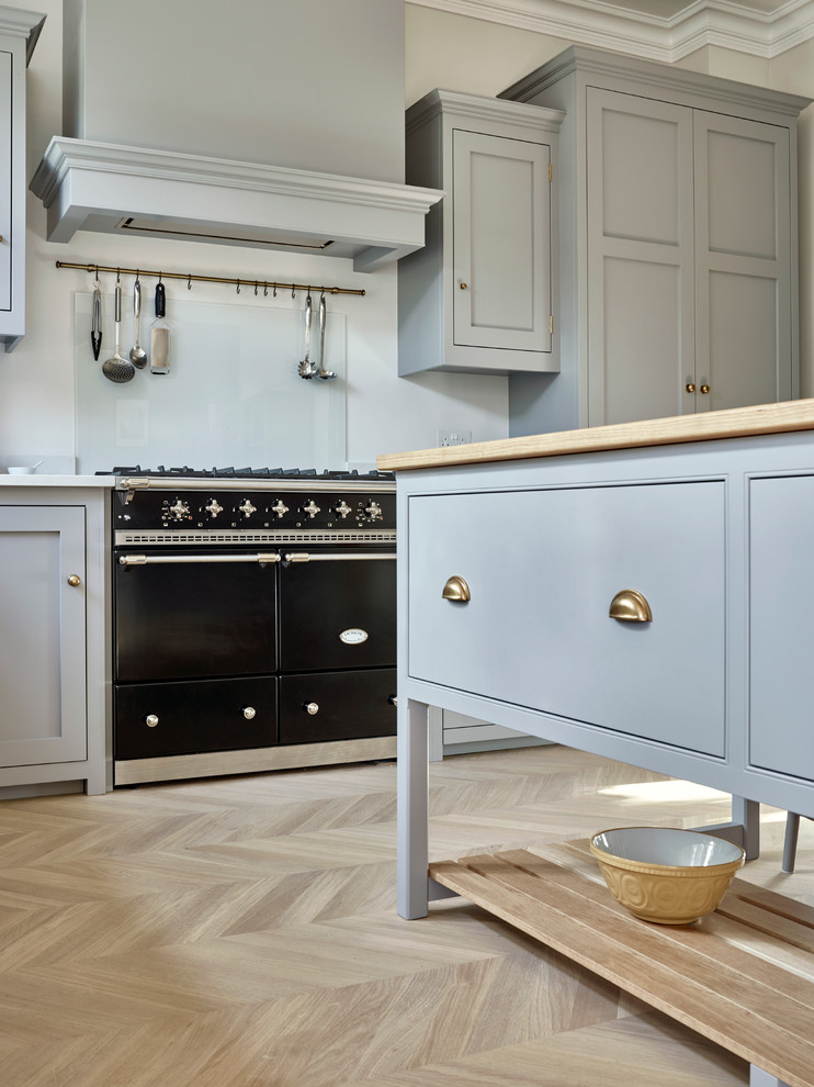 Ejemplo de cocina clásica renovada con fregadero sobremueble, armarios estilo shaker, puertas de armario grises, suelo de madera clara y una isla