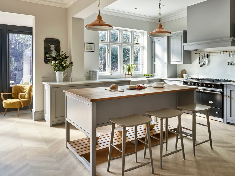 This is an example of a classic l-shaped kitchen/diner in London with a belfast sink, grey cabinets, light hardwood flooring, an island and shaker cabinets.