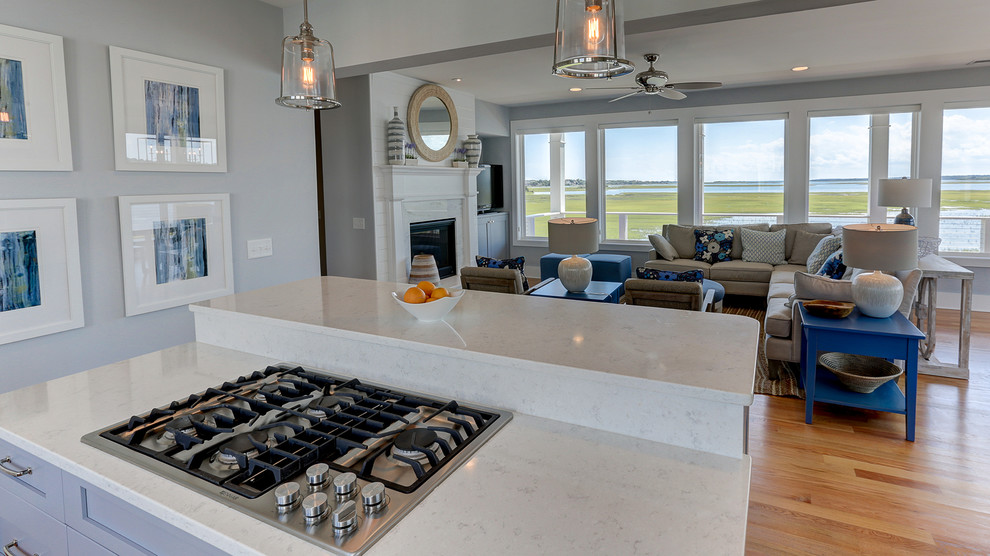 Immagine di un cucina con isola centrale costiero con lavello sottopiano, ante blu, paraspruzzi con piastrelle di vetro, elettrodomestici in acciaio inossidabile, parquet chiaro e pavimento marrone