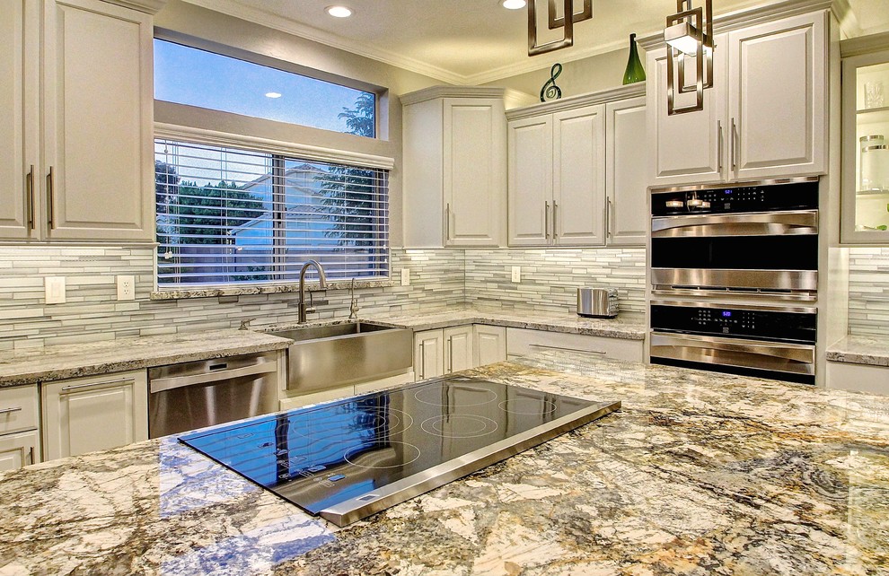 Example of a large minimalist u-shaped ceramic tile eat-in kitchen design in Phoenix with a farmhouse sink, raised-panel cabinets, white cabinets, granite countertops, white backsplash, glass tile backsplash, stainless steel appliances and an island