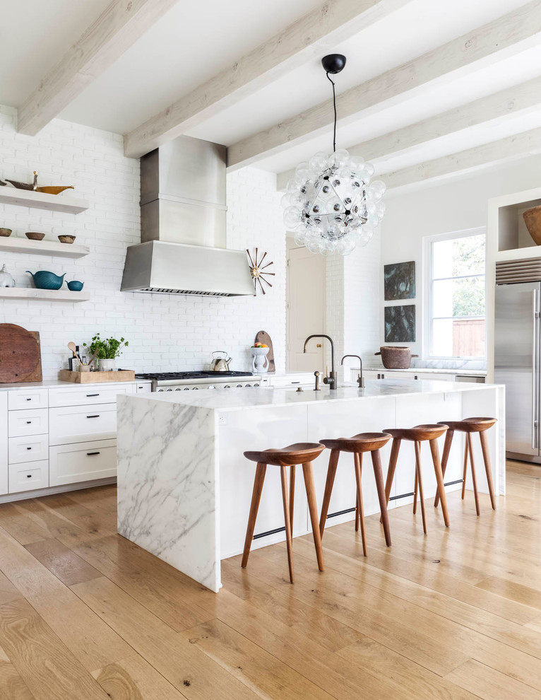 Traditional kitchen in Dallas with shaker cabinets, white cabinets, white splashback, an island, metro tiled splashback, stainless steel appliances and light hardwood flooring.