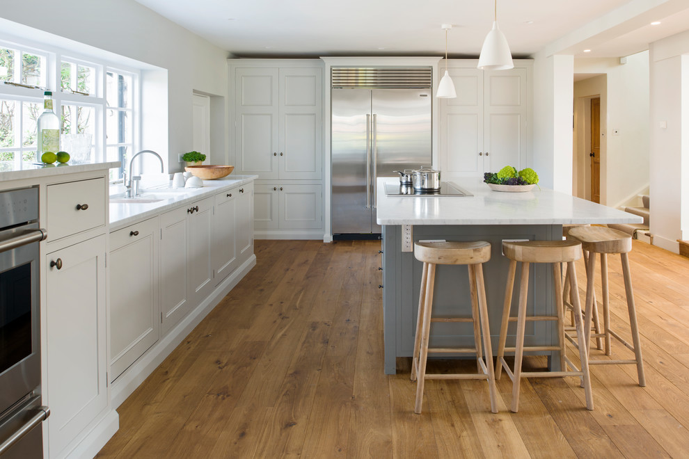 Klassische Küche mit Kassettenfronten, weißen Schränken, Küchengeräten aus Edelstahl, hellem Holzboden, Kücheninsel und weißer Arbeitsplatte in Sussex