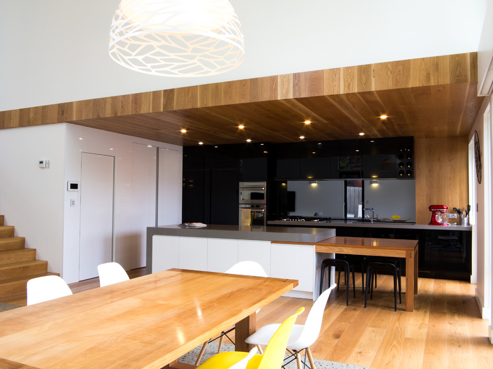 Bild på ett stort funkis kök, med svarta skåp, bänkskiva i kvarts, stänkskydd med metallisk yta, spegel som stänkskydd, rostfria vitvaror, mellanmörkt trägolv och en köksö