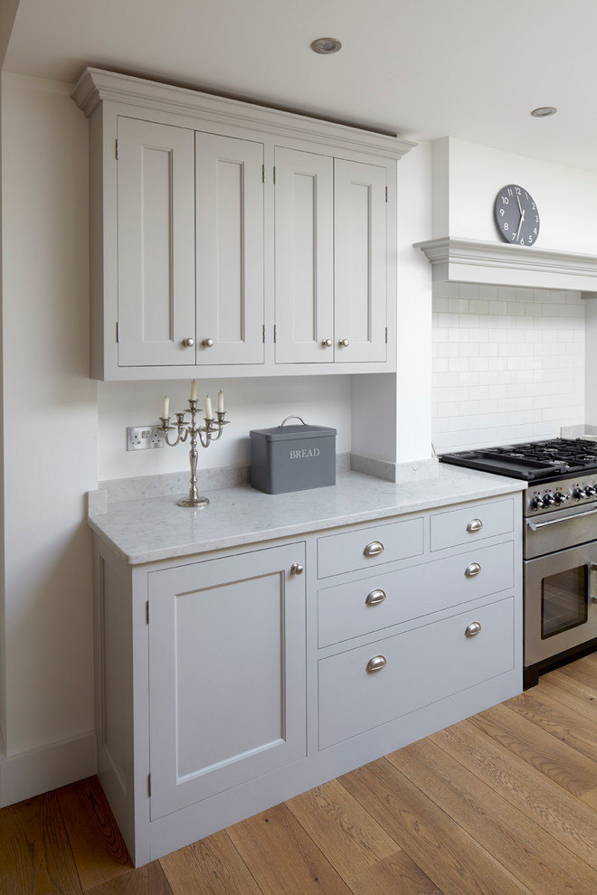 This is an example of a large classic l-shaped open plan kitchen in London with a double-bowl sink, shaker cabinets, grey cabinets, composite countertops, white splashback, metro tiled splashback, stainless steel appliances, medium hardwood flooring and an island.