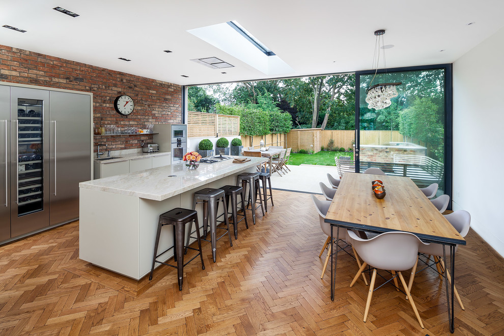 This is an example of a contemporary galley kitchen/diner in Surrey with marble worktops, red splashback, stainless steel appliances, medium hardwood flooring, an island and white cabinets.