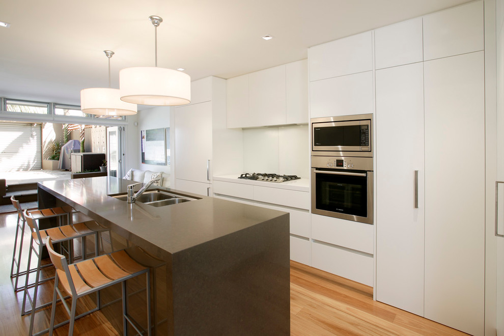 Eat-in kitchen - small contemporary l-shaped light wood floor eat-in kitchen idea in Sydney with an undermount sink, flat-panel cabinets, white cabinets, quartzite countertops, white backsplash, glass sheet backsplash, stainless steel appliances and an island