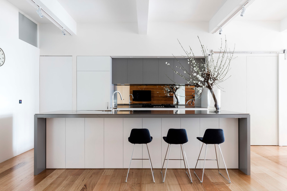 Foto på ett mellanstort funkis kök, med en integrerad diskho, bänkskiva i rostfritt stål, spegel som stänkskydd, rostfria vitvaror, ljust trägolv och en köksö
