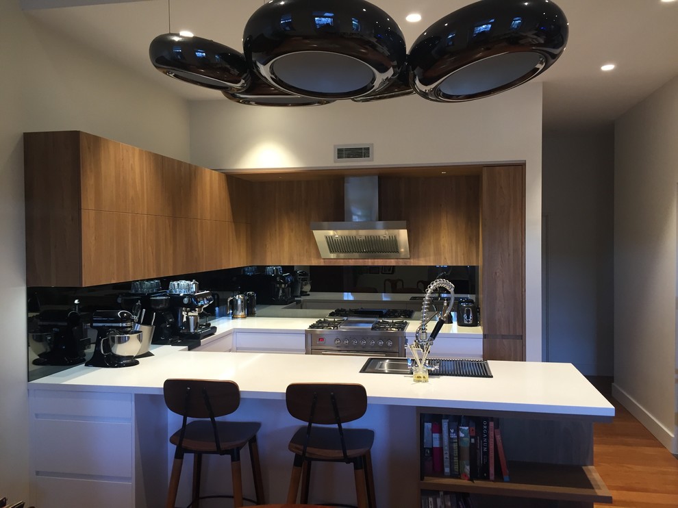 Eat-in kitchen - mid-sized modern u-shaped medium tone wood floor eat-in kitchen idea in Sydney with a double-bowl sink, shaker cabinets, medium tone wood cabinets, solid surface countertops, black backsplash, mirror backsplash, stainless steel appliances and an island