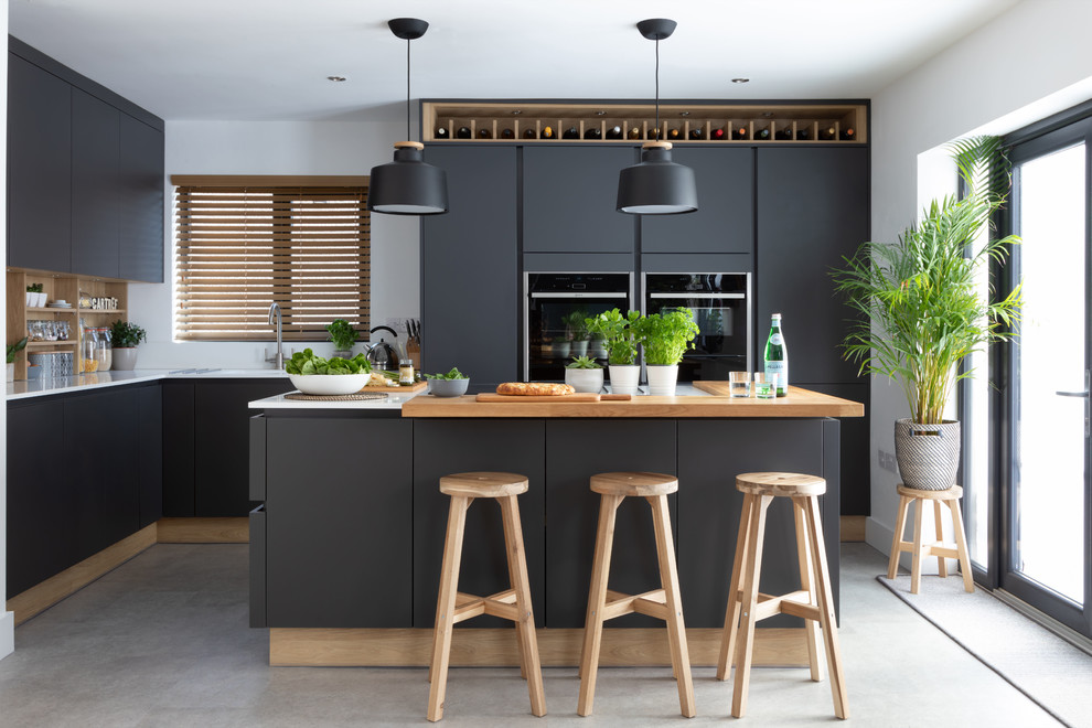 Skandinavische Küche in L-Form mit flächenbündigen Schrankfronten, schwarzen Schränken, schwarzen Elektrogeräten, Kücheninsel, grauem Boden und weißer Arbeitsplatte in Sonstige